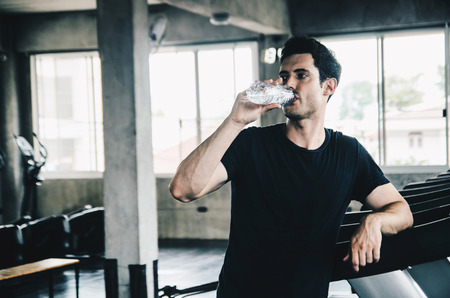 Unrecognizable young man in sportswear running on treadmill at gym and holding bottle of waterの写真素材