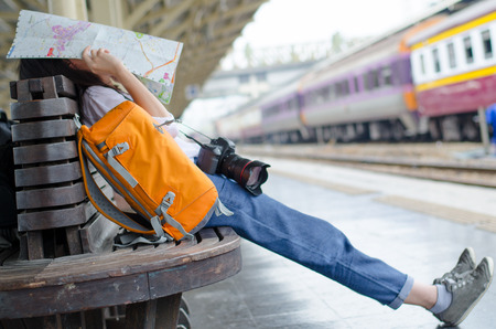 girl leaning on a wooden chair, backpack, sitting at the train station. A map in her hands.の写真素材