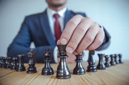 Retro style image of a businessman with clasped hands planning strategy with chess figures on an old wooden table.の写真素材
