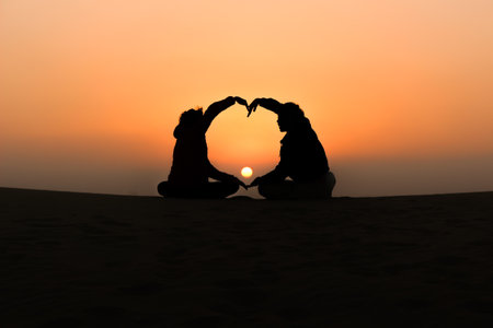 silhouette of a young couple making a heart with their arms at sunsetの写真素材