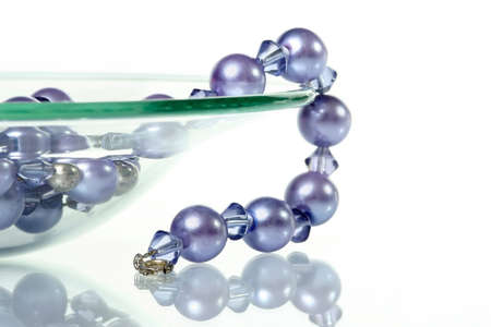 Purple necklace hanging from glass bowl on white backgroundの写真素材
