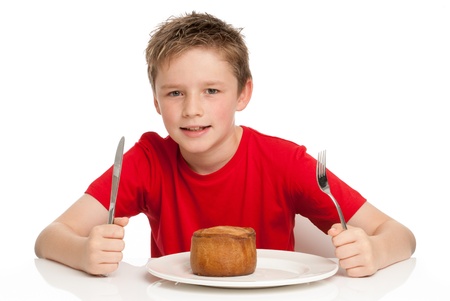 Young boy eating a tasty pork pie with a knife and fork. Isolated on a white background.の写真素材