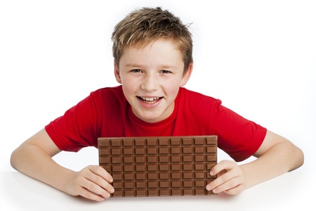 Cute smiling young boy eating a very big bar of chocolate. Wearing a red T-shirt, shot in the studio on a white background.の写真素材