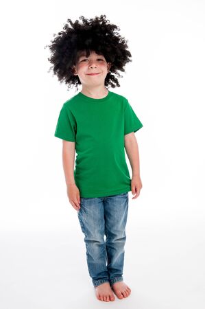 Full length young smiling boy standing in studio on white background with a big black funny wig.の写真素材
