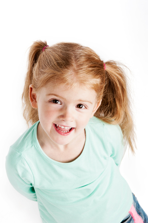 Smiling little girl looking up at camera. Studio portrait, isolated on white background.の写真素材