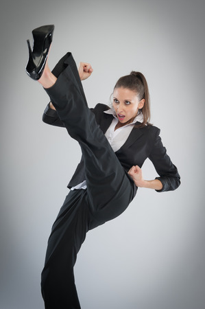 Agressive woman in high heels kicking into the air. Martial Art Karate pose in the studio on grey background.の写真素材