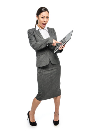 Smart woman in grey business suit pointing her finger at a big calculator. Studio shot on white background.の写真素材
