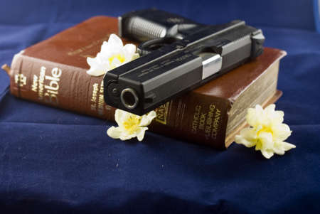 A black gun resting on a closed bible with flowersの写真素材