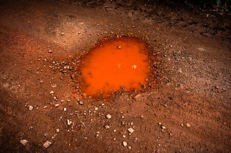 Small red color puddle on forest footway, soil contains iron, therefore water is red.の写真素材