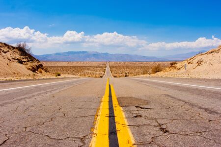 Big dip in the road along a desert highway  Clouds and mountains in the background の写真素材
