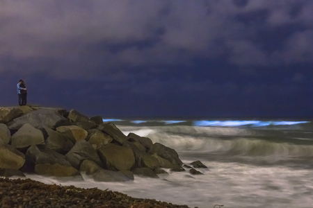 A couple hugs each other while watching the bioluminescent tide glow blue in San Diego, California.の写真素材