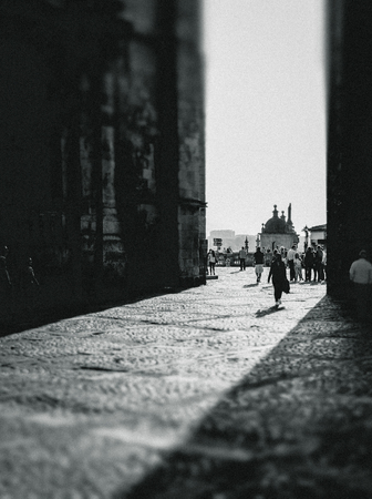 Black and white image of an old town square in Porto, Portugal with people walking between tall building walls towards a domed building in the sunshine beyondの写真素材