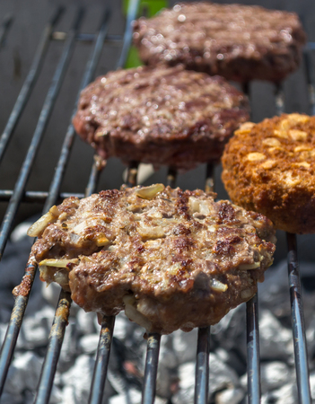 Close up of a beef burger filled with onions and veggie burger off to the side on bbq
