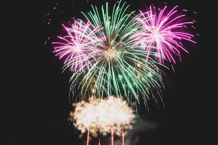Green and purple fireworks mid explosion against a dark night sky