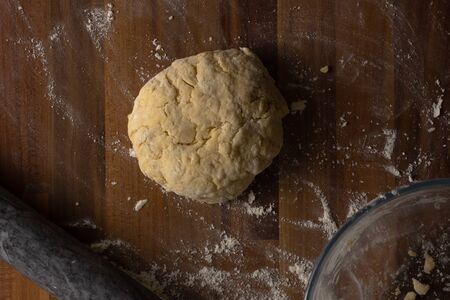A top view of cheese scone dough rolled into a ball on a wooden surface surrounded by flour, a rolling pin and a clear glass bowlの写真素材