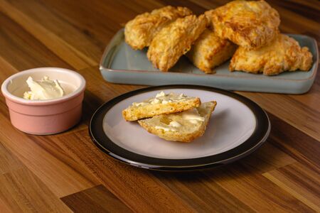 Cheese scones sitting on a plate surrounded by a pink butter dish and a blue plate containing stacks of cheese sconesの写真素材
