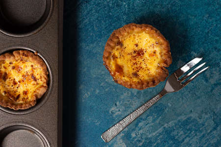 A freshly baked egg custard tart from above with a cake fork laid to the side and a baking tray...