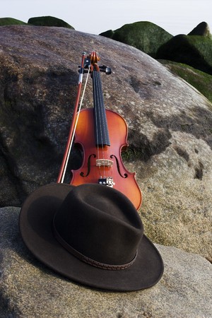 Wide angle view of Violin and cowboy hat lying on a boulder by the Oceanの写真素材