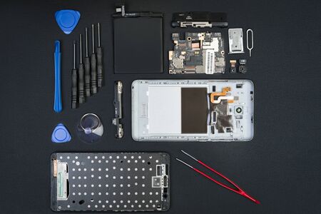 The disassembled smartphone with the removed screen and special purpose tools on the black desktop. Cell phone details in flatlay style.の写真素材