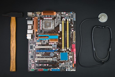 Fix or break a broken computer. Motherboard, hammer and stethoscope on a black table. Top view.の写真素材