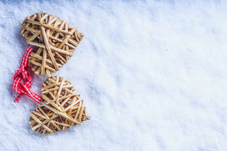Two beautiful romantic vintage entwined beige flaxen hearts tied together with a ribbon on a white snow winter background. Love and St. Valentines Day concept.の写真素材