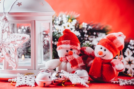Cute couple of little adorable snowmen is standing near the white fairy lantern with a toy heart on it and decorated fir tree branch behind it. Christmas card with copy space for your text.の写真素材