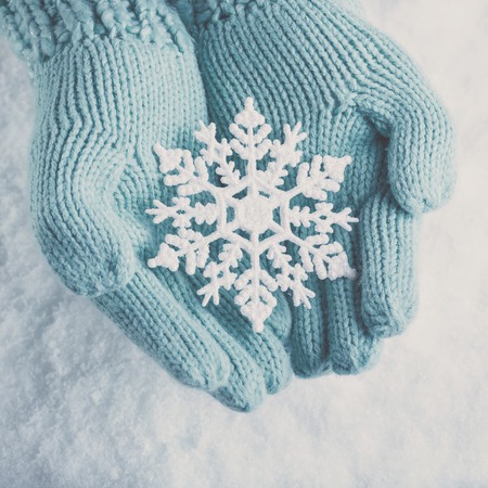 Female hands in light teal knitted mittens with sparkling wonderful snowflake on a white snow background. Winter and Christmas concept.の写真素材