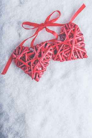 Two beautiful romantic vintage red hearts tied together with a ribbon on a white snow winter background. Love and St. Valentines Day concept.の写真素材