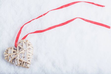 Beautiful magical vintage beige heart tied with a red ribbon on a white snow background. Winter and Christmas concept.の写真素材
