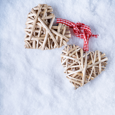 Two beautiful romantic vintage entwined beige flaxen hearts tied together with a ribbon on a white snow winter background.の写真素材