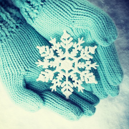 Female hands in light teal knitted mittens with sparkling wonderful snowflake on a white snow background.の写真素材