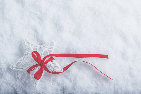 Beautiful magical vintage white star tied with a red ribbon on a white snow background.の写真素材