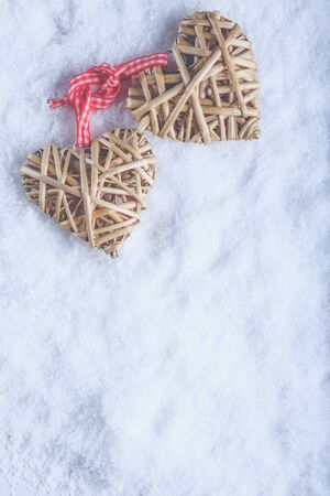 Two entwined beige flaxen hearts tied together with a ribbon on white snow.の写真素材