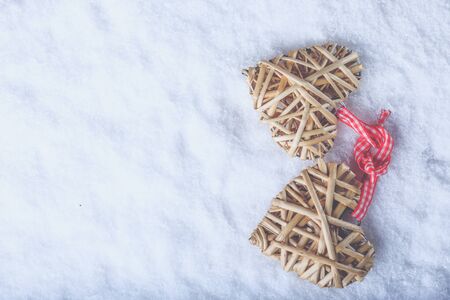 Two entwined beige flaxen hearts tied together with a ribbon on white snow.の写真素材
