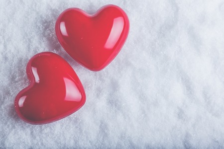 Two red glossy hearts on a frosty white snow winter background.の写真素材