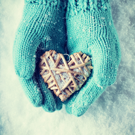 Female hands in teal knitted mittens with a entwined vintage romantic heart on a snow background.の写真素材