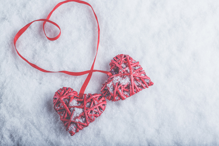 Two beautiful romantic vintage red hearts tied together with a ribbon on a white snow winter background.の写真素材