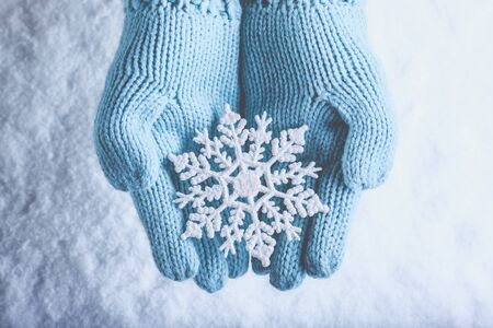 Female hands in light teal knitted mittens with snowflake on snow background.の写真素材