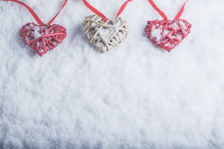 Three vintage hearts are hanging on a red band on a white snow winter background.の写真素材