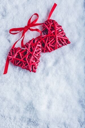 Two beautiful romantic vintage red hearts tied together with a ribbon on a white snow winter background.の写真素材