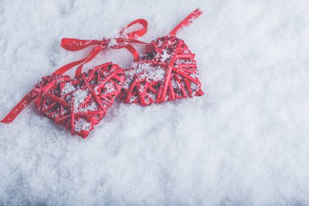 Two beautiful romantic vintage red hearts tied together with a ribbon on a white snow winter background.の写真素材