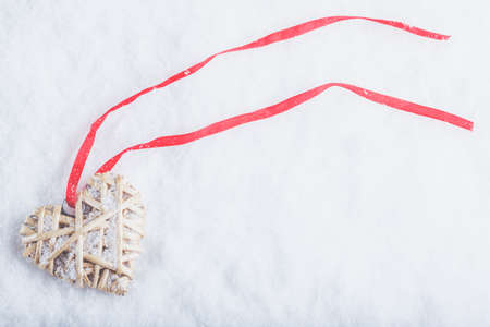 Beautiful magical vintage beige heart tied with a red ribbon on a white snow background.の写真素材