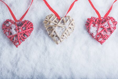 Three vintage hearts are hanging on a red band on a white snow winter background.の写真素材