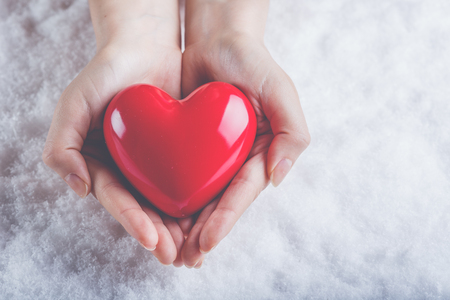 Woman hands are holding a beautiful glossy red heart in a snow winter background.の写真素材