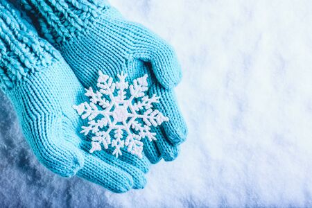 Female hands in light teal knitted mittens with snowflake on snow background.の写真素材