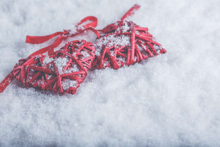 Two beautiful romantic vintage red hearts tied together with a ribbon on a white snow winter background.の写真素材