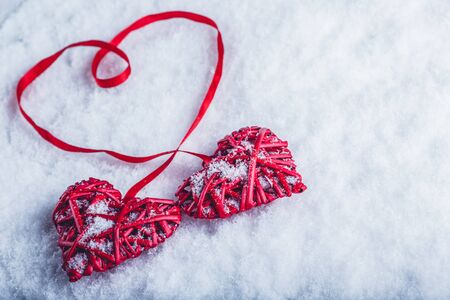 Two beautiful romantic vintage red hearts tied together with a ribbon on a white snow winter background.の写真素材