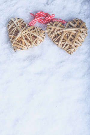 Two beautiful romantic vintage entwined beige flaxen hearts tied together with a ribbon on a white snow winter background.の写真素材