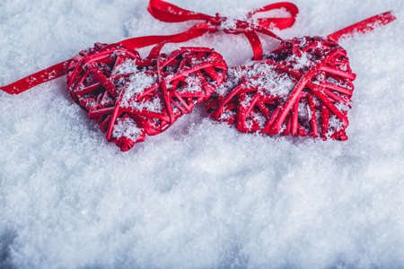 Two beautiful romantic vintage red hearts tied together with a ribbon on a white snow winter background.の写真素材