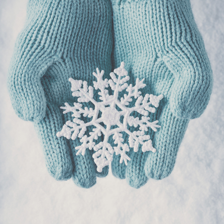 Female hands in light teal knitted mittens with sparkling wonderful snowflake on a white snow background.の写真素材